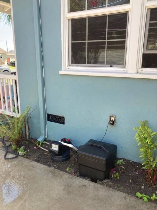 Low-profile outdoor water treatment system tucked against home exterior